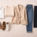Minimal capsule wardrobe flat lay showing versatile wardrobe basics including a white shirt, knit sweater, blazer, jeans, skirt, boots, and sneakers arranged in a structured layout.