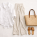 Coastal grandmother aesthetic outfit flat lay featuring white linen shirt, beige wide-leg trousers, leather sandals, and straw tote on a neutral background.