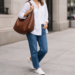 Woman wearing a relaxed everyday outfit with a slouchy brown leather hobo bag on shoulder, styled with white oversized shirt and straight-leg jeans on a clean city street.