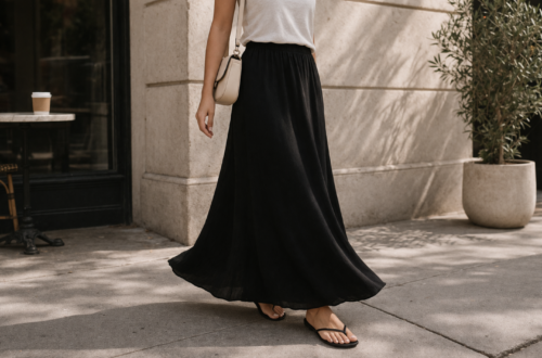 Woman wearing a black maxi skirt styled with a simple white top and minimal sandals showing the full-length ankle silhouette of a classic maxi skirt.