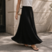 Woman wearing a black maxi skirt styled with a simple white top and minimal sandals showing the full-length ankle silhouette of a classic maxi skirt.