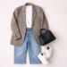 Model off duty style flat lay outfit featuring oversized neutral blazer, white T-shirt, straight-leg jeans, white sneakers and structured handbag on a minimal beige background.