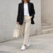 Woman wearing a minimalist Scandinavian outfit with oversized blazer, white t-shirt, straight-leg trousers and sneakers in a neutral-toned setting.