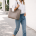 Woman carrying a structured leather tote bag styled with a white button-down shirt, straight-leg jeans and loafers in an effortless everyday outfit.